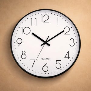 Könnte beinhalten: Eine runde Wanduhr mit weißem Zifferblatt und schwarzen Ziffern und Zeigern. Die Uhr hat einen schwarzen Rahmen und das Wort "QUARTZ" ist unten aufgedruckt. Die Uhr hat einen Durchmesser von etwa 25 cm.