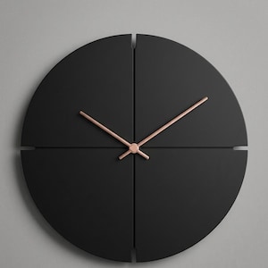 May include: A modern, minimalist wall clock. The clock face is divided into four black quadrants with a copper-colored center and hands. The hands are thin and elegant, indicating the time. The clock is mounted on a gray wall.