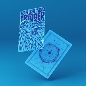 May include: Two blue playing cards with a fantasy owl illustration and text that reads "WAN SHI TONG TRIGGER". The back of the card has a geometric design with a central symbol. The cards are set against a blue background.