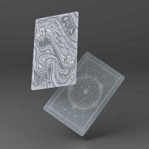 May include: Two gray playing cards. One card features a detailed illustration of a monster with the word "TOKEN" and "COPY" in a stylized font. The other card has a circular design with geometric patterns.