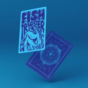 Może przedstawiać: Dwie niebieskie karty do gry. Jedna przedstawia ilustrację ryby i słowa "FISH TRIGGER". Druga karta ma geometryczny wzór na odwrocie. Karty są umieszczone na niebieskim tle.
