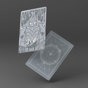 May include: Two rectangular playing cards in a monochromatic gray color scheme. The front card features a stylized illustration of a mechanical figure with the text CONSTRUCT and +1/+1 FOR EACH ARTIFACT. The back card displays a geometric design.