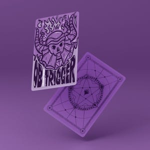 Op de afbeelding: Twee paarse speelkaarten met een fantasiethema. Eén kaart toont een schedel met hoorns en het woord "OBTRIGGER". De andere kaart heeft een geometrisch ontwerp met een centrale ster. De kaarten zweven tegen een paarse achtergrond.