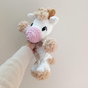 May include: A handmade, plush giraffe toy. The giraffe is primarily white with brown and tan accents. It has a pink nose, black eyes, and a fluffy mane. The toy is soft and cuddly, perfect for children.