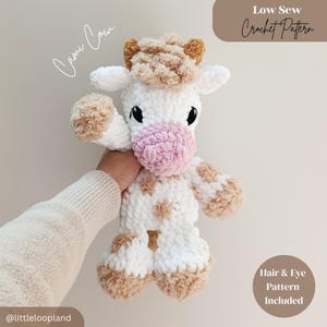 Könnte beinhalten: Ein handgefertigtes Häkeltier in Form einer Kuh in Weiß, Beige und Rosa. Das Kuscheltier hat schwarze Augen und eine rosa Nase. Der Text "Cami Cow" ist kursiv geschrieben. Das Bild enthält auch den Text "Low Sew Crochet Pattern" und "Hair & Eye Pattern Included".