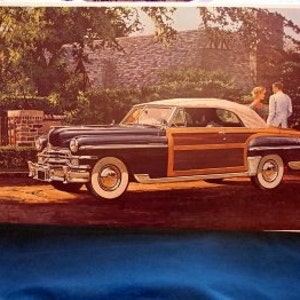 May include: A vintage dark blue and wood-paneled station wagon with a white convertible top. The car is parked on a dirt driveway in front of a stone house.