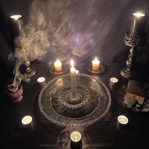 Può includere: Una scena poco illuminata con candele accese di varie dimensioni e forme, disposte su una superficie scura. Il fumo si alza da un bruciatore di incenso decorativo. La composizione include un grande vassoio d'argento ornato e candelabri.
