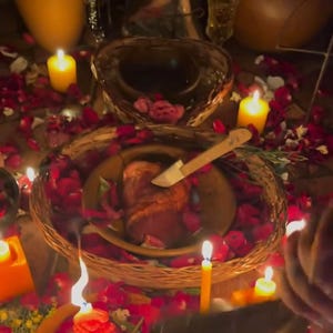 Puede incluir: Una escena con poca luz con una cesta tejida que contiene un plato con un trozo de carne y un cuchillo. La cesta está rodeada de pétalos de rosas rojas y velas encendidas. Se ve una segunda cesta.