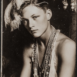 Puede incluir: Retrato en tonos sepia de una persona adornada con un tocado de plumas y múltiples collares de perlas. La persona lleva también una prenda de encaje delicado. La imagen tiene una estética vintage, con iluminación suave y enfoque en la expresión del sujeto.