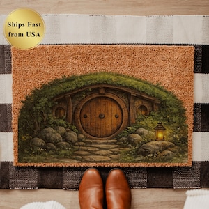 May include: A rectangular doormat featuring a hobbit hole design with a round wooden door, stone path, and a lantern. The mat has a brown background and is surrounded by green foliage. The text "Ships Fast from USA" is in a gold circle.