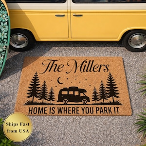 May include: A rectangular doormat with a natural coir fiber texture. The black design features the text "The Millers", a camper van, pine trees, a crescent moon, and the phrase "HOME IS WHERE YOU PARK IT". A yellow and white van is in the background.