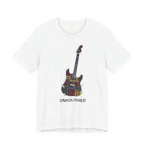 Può includere: T-shirt bianca con un design di chitarra patchwork colorata. La grafica della chitarra include motivi a quadri rossi, gialli e verdi. La parola "UNPOLISHED" è stampata sotto in nero.