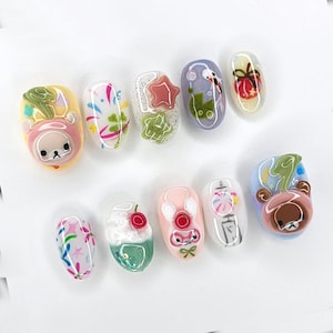 Peut inclure: Dix faux ongles avec des motifs uniques. Les motifs comprennent des personnages de dessins anim&eacute;s, des &eacute;toiles, des n&oelig;uds et des motifs floraux. Les couleurs incluent le rose, le blanc, le jaune, le vert et le bleu. Les ongles sont ovales et ont une finition brillante.