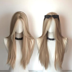 Puede incluir: Dos cabezas de maniquí con pelucas rubias largas con raíces oscuras y reflejos. Un maniquí tiene gafas de sol negras encima de la peluca. Ambos maniquíes llevan gargantillas negras con tachuelas. Las pelucas tienen un corte en capas.