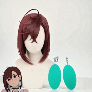 Op de afbeelding: Een bordeauxrode pruik met een stompe bob-cut wordt getoond op een mannequinhoofd. Twee grote, ovale, turquoise oorbellen hangen naast de pruik. Een cartoonafbeelding van een persoon met bijpassende oorbellen staat in de linkerbenedenhoek.