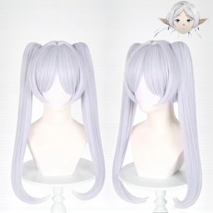 Puede incluir: Dos pelucas de color púrpura claro con largas coletas se exhiben en cabezas de maniquí blancas. Las pelucas tienen flequillo y están peinadas para enmarcar la cara. Una pequeña ilustración de un personaje con orejas puntiagudas está en la esquina superior derecha.