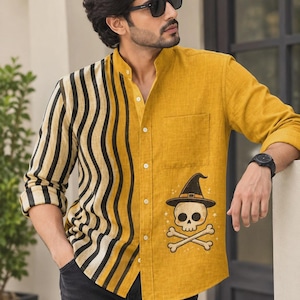 Pode incluir: Uma camisa de manga comprida com botões, de cor amarelo-mostarda, com um padrão de riscas verticais onduladas pretas e creme no lado direito. O lado esquerdo inclui um bolso no peito e um estampado gráfico de um crânio com chapéu.