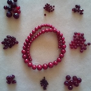May include: Assortment of red and purple beads in various sizes and shapes, including a long strand of large, round beads.