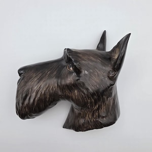 May include: A ceramic sculpture of a Scottish Terrier dog head. The dog's fur is a dark brown with lighter brown highlights. The sculpture has pointed ears and a detailed snout, set against a white background.