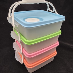May include: A stackable lunch container set with four colorful compartments. The containers have pastel blue, green, pink, and orange lids. A white handle arches over the top for easy carrying. The containers are made of plastic.