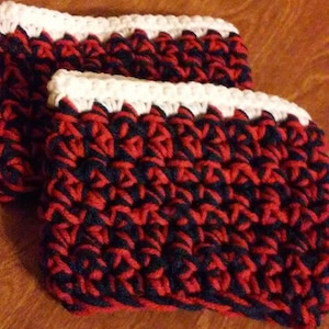 May include: Two crocheted cup cozies in red, black, and white. The cozies are made with a textured stitch and have a white border.