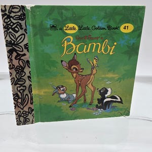 May include: A vintage Little Golden Book titled "Bambi." The cover features a green background with illustrations of Bambi, a butterfly, a rabbit, and a skunk. The book's spine has a black and white floral pattern.