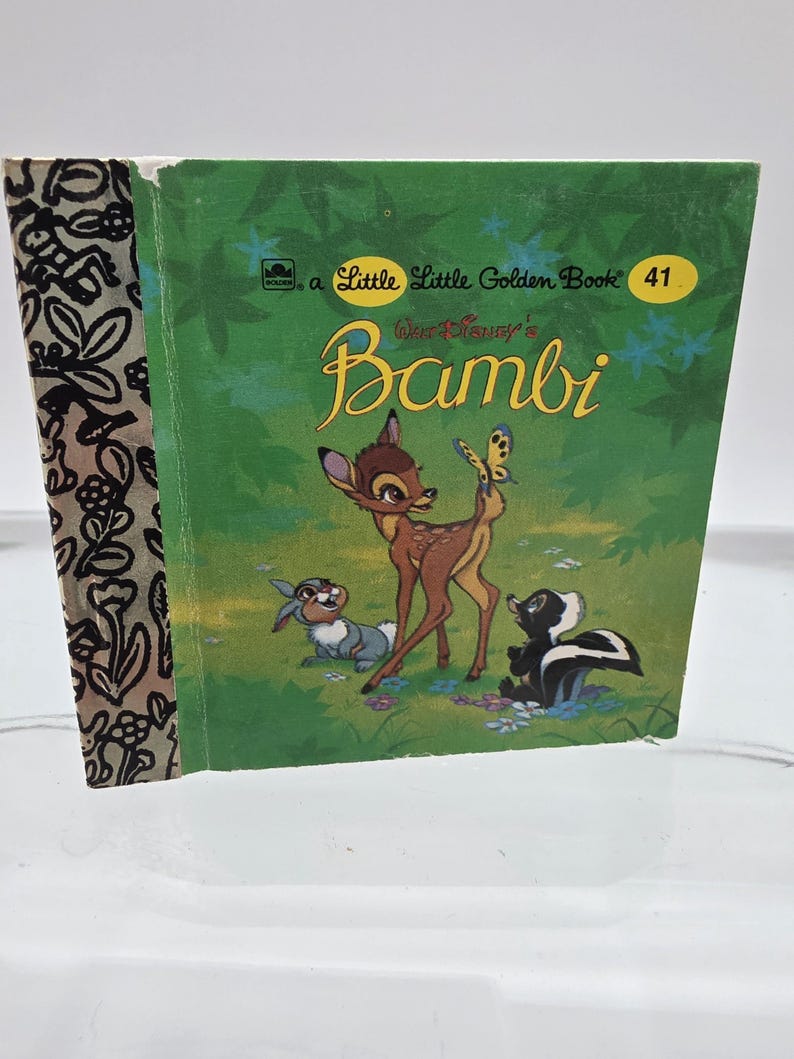 May include: A vintage Little Golden Book titled "Bambi." The cover features a green background with illustrations of Bambi, a butterfly, a rabbit, and a skunk. The book's spine has a black and white floral pattern.