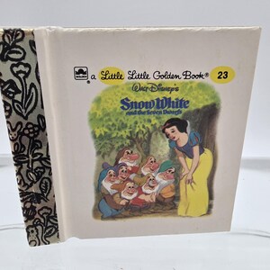 May include: A Little Golden Book titled "Snow White and the Seven Dwarfs." The cover features an illustration of Snow White in a yellow dress with the seven dwarfs. The book's spine has a black and white floral pattern.