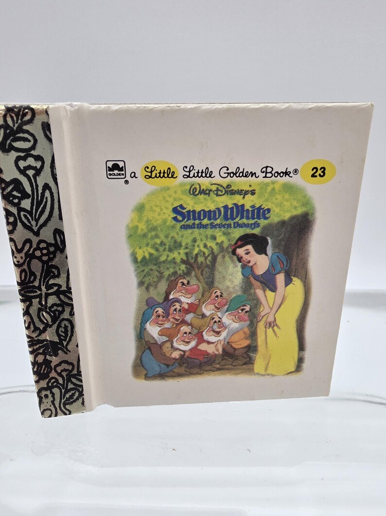 May include: A Little Golden Book titled "Snow White and the Seven Dwarfs." The cover features an illustration of Snow White in a yellow dress with the seven dwarfs. The book's spine has a black and white floral pattern.