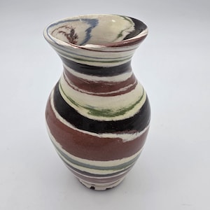 May include: A ceramic vase with a wide, striped pattern in shades of brown, black, white, green, and blue. The vase has a rounded body and a flared rim. The vase is approximately 7 inches tall.