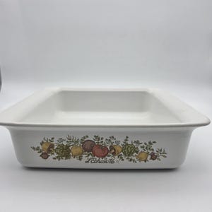 May include: A rectangular white ceramic baking dish featuring a decorative botanical illustration of various vegetables and herbs along the front side. The text L'Echalote is printed in a script font below the colorful produce graphic.