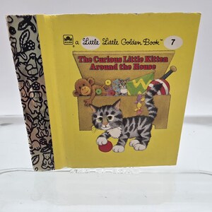 May include: A Little Golden Book titled "The Curious Little Kitten Around the House." The cover is yellow with an illustration of a gray and white kitten playing with a red ball. The book's spine has a patterned design.