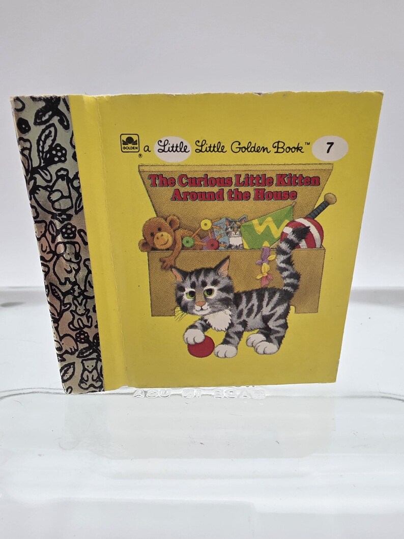 May include: A Little Golden Book titled "The Curious Little Kitten Around the House." The cover is yellow with an illustration of a gray and white kitten playing with a red ball. The book's spine has a patterned design.