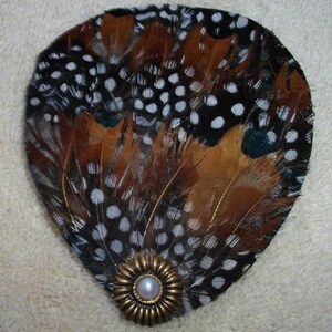 May include: A brown, black, and white feathered hair clip with a pearl and gold accent.