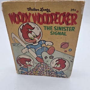 May include: Vintage "Woody Woodpecker: The Sinister Signal" comic book. The cover features Woody Woodpecker in a space suit, with the title in red and green. The comic book is in a tan color.