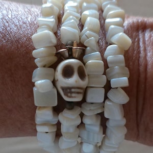 May include: A multi-strand bracelet featuring white, irregular-shaped beads. A central skull charm with a crown adds a unique focal point. The bracelet is designed to be worn on the wrist.