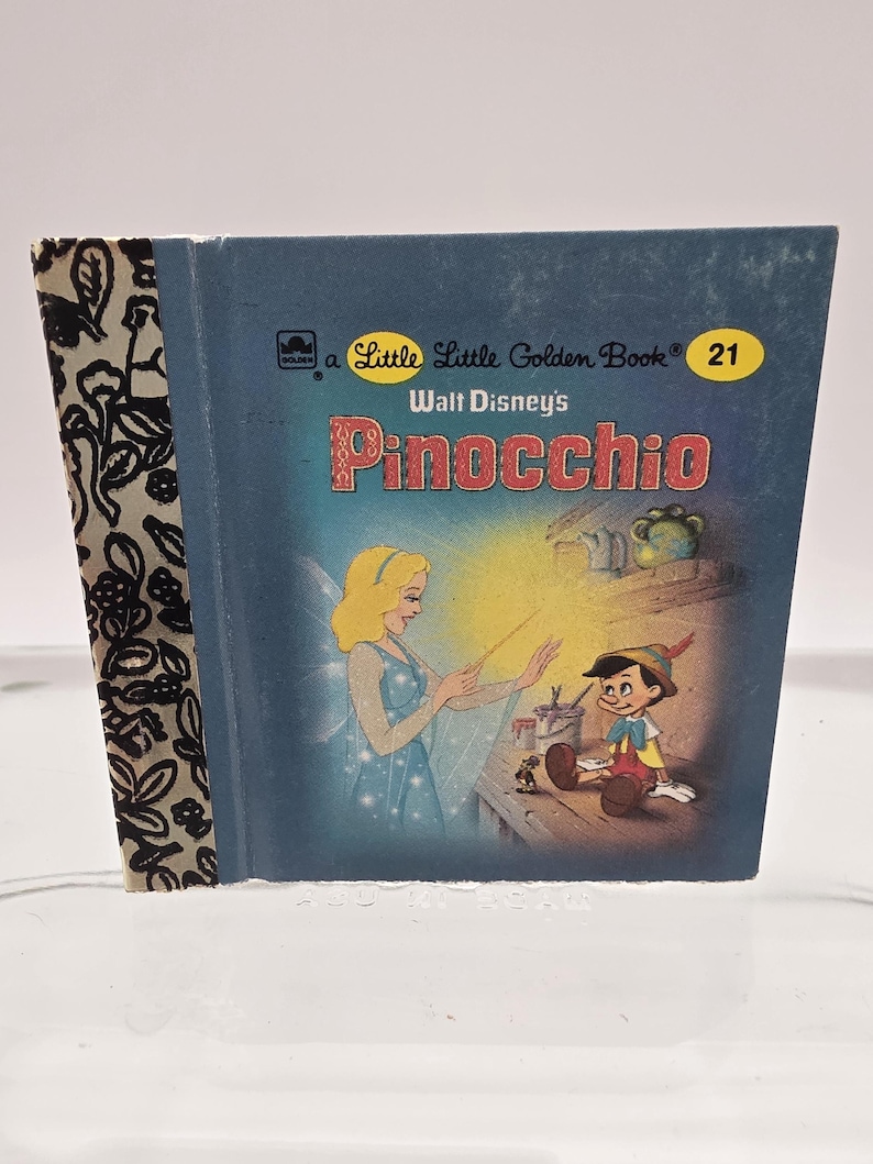 May include: A vintage Little Golden Book titled "Pinocchio" by Walt Disney. The cover is blue with illustrations of Pinocchio and a fairy. The spine has a black and white floral pattern. The book is number 21 in the series.