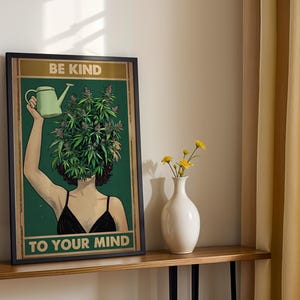 Könnte beinhalten: Gerahmter Kunstdruck mit einer Frau mit einem Kopf aus Cannabispflanzen, die eine Gießkanne hält. Der Druck trägt den Text "BE KIND TO YOUR MIND" in goldener Schrift auf grünem Hintergrund. Die Frau trägt ein schwarzes Oberteil.