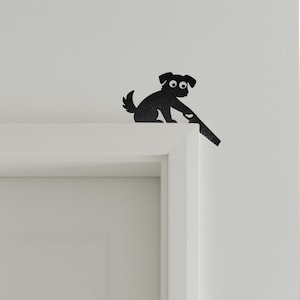 Könnte beinhalten: Schwarze Silhouette eines Hundes mit großen Augen, der auf einem weißen Türrahmen sitzt. Der Hund scheint eine Säge zu halten. Der Hund ist ein dekorativer Gegenstand, möglicherweise eine Wand- oder Türdekoration.