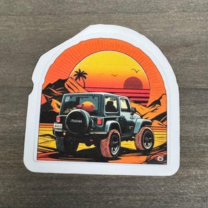 May include: A sticker depicting a dark green Jeep with a spare tyre, set against a sunset with mountains and palm trees. The Jeep has red tyres. The word "Jessel" is on the spare tyre.