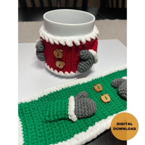Peut inclure: Manchon de tasse et dessous de tasse assortis en crochet, en rouge, blanc et vert, avec des mitaines grises et des boutons en bois. Le manchon est en forme de costume de Père Noël. Téléchargement numérique.