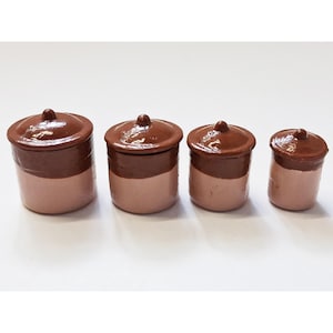 May include: A set of four cylindrical ceramic canisters with lids, arranged in descending order of size. Each canister features a glossy dark brown glaze on the upper portion and lid, with a smooth light tan finish on the lower body section.