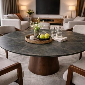 May include: A round dining table with a dark gray marble top and a dark brown wooden base. The table is surrounded by four chairs with light gray upholstered seats and wooden frames. A tray with fruit and a candle sits on the table.