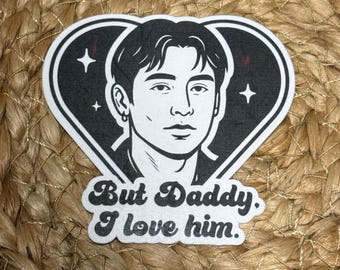 Op de afbeelding: Zwart-witte sticker met een gestileerde afbeelding van een gezicht in een hartvorm. De tekst "But Daddy, I love him" staat eronder. De sticker heeft een witte achtergrond.