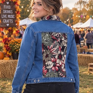 May include: A blue denim jacket featuring a large rectangular back panel with a floral tapestry print in shades of red, green, and cream. The jacket includes a matching floral print collar, long sleeves with button cuffs, and a button-front closure.