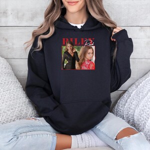 May include: Black hoodie featuring a graphic of a woman with the name "Riley Reid" in red script. The graphic includes two images of the woman. The hoodie has a drawstring hood and a kangaroo pocket.