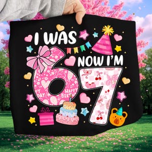 Puede incluir: Gráfico de cumpleaños negro con el texto "I WAS 6 NOW I'M 7". El número 6 es rosa con un lazo, corazones y estrellas. El número 7 es rosa y blanco a cuadros con cerezas. Incluye un pastel, un regalo y un oso.