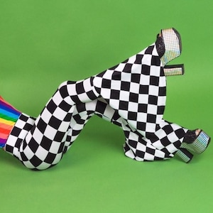 May include: A person wearing a rainbow striped swimsuit and black and white checkered flared pants. The person is lying on a green background.