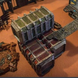 Könnte beinhalten: Ein detailliertes Miniatur-Geländestück für Tabletop-Spiele. Das Stück weist ein modulares Design mit einer Kombination aus roten, grünen und grauen Metallkomponenten auf. Das Design umfasst einen Steg und Lagercontainer, perfekt für ein Science-Fiction- oder Industrie-Setting.