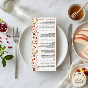 May include: A rectangular Rosh Hashanah Simanim card featuring a floral border with red, orange, and green flowers. The card includes English and Hebrew text listing traditional foods like apples, honey, pomegranate, and fish with their blessings.